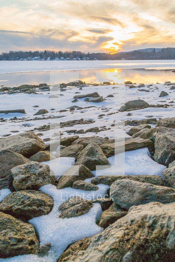 snow on rocks along a shore at sunset 