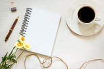 blank pages in a notebook, pen, clip, coffee cup, twine, spring flower on a white background 