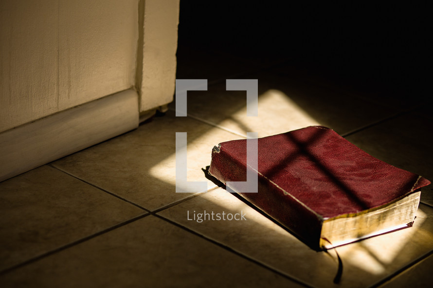 a Bible lying in sunlight on the floor 