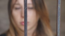 Woman out of focus staring into camera behind metal bars.
