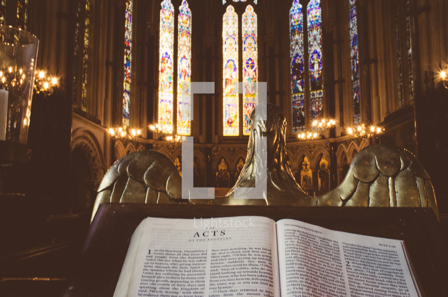 Bible open to Acts in a cathedral with stained glass.