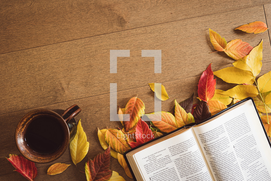 Open bible and a cup of coffee with a fall leaf border on wood