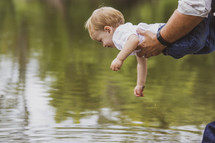 father holding his son over pond water