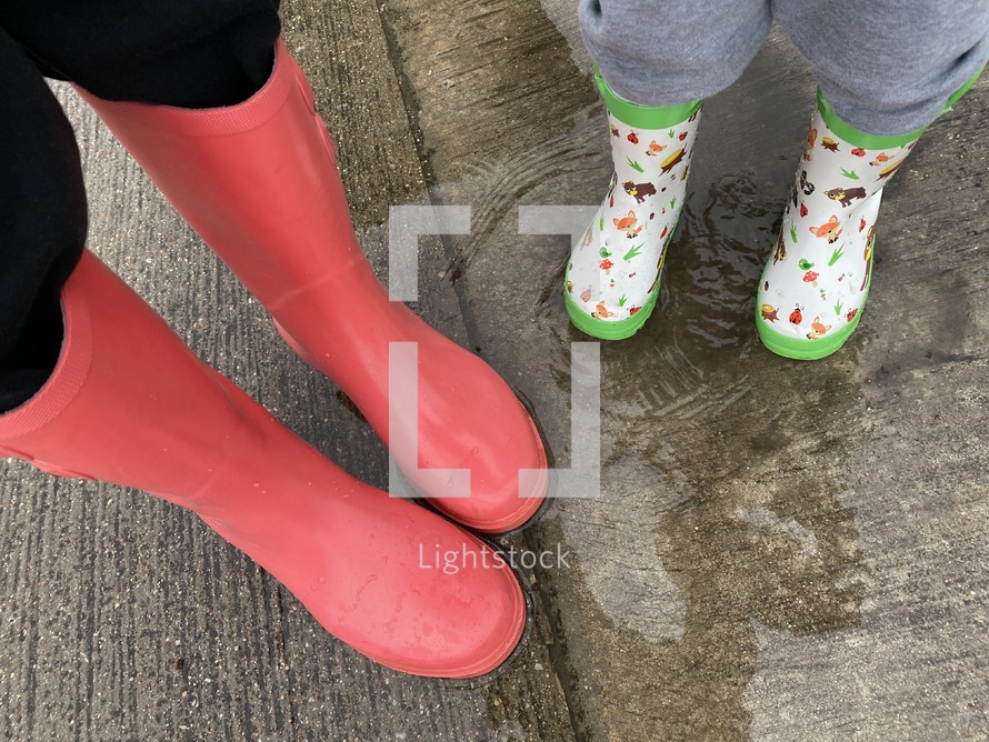 mother or grandmother and child or siblings in rain boots standing in a puddle