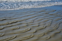tide flowing over ripples in sand on a beach 