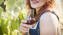 Beautiful red hair girl smile with glass of wine among vineyards in countryside