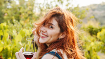 Beautiful red hair girl smile and walk with glass of wine among vineyards