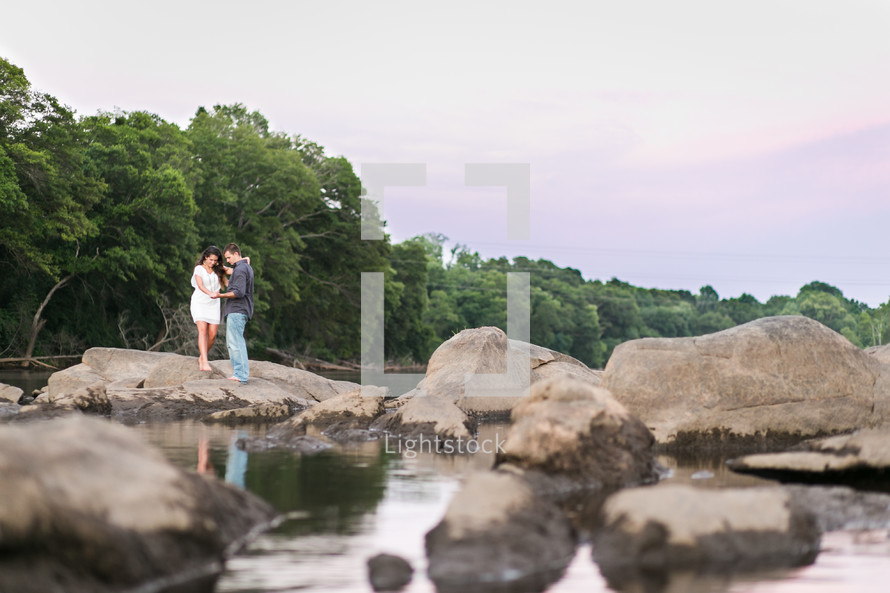 coupe standing on rocks on a shore holding hands 