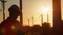 Silhouette of Engineer against wind power plant generator at sunset