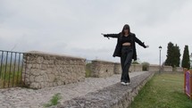 Woman With Black Clothes Walks Balanced On The Wall Outside