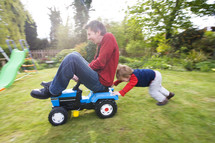 Son pushing his father on a toy tractor in their back garden themes of exhilaration family bonding