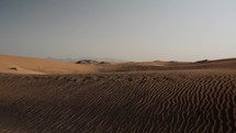 Distant mountains in middle eastern desert, nature landscape. Sand blowing in wind over desert sand dunes in evening desert sunset, sunlight in cinematic slow motion.