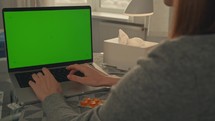 Woman using a laptop with medicine and facial tissues nearby