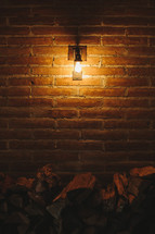 Patio light on brick wall over stack of firewood.