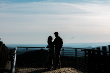 a couple standing on a balcony overlooking a mountain 