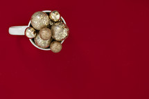 gold Christmas ornaments in a mug on a red background 