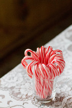 candy canes in a glass on a lace tablecloth 