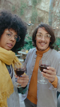 Cheerful Latin couple holding wine and talking on camera, making selfie or video calling during barbecue party in the backyard. POV shot, video portrait. Vertical format footage
