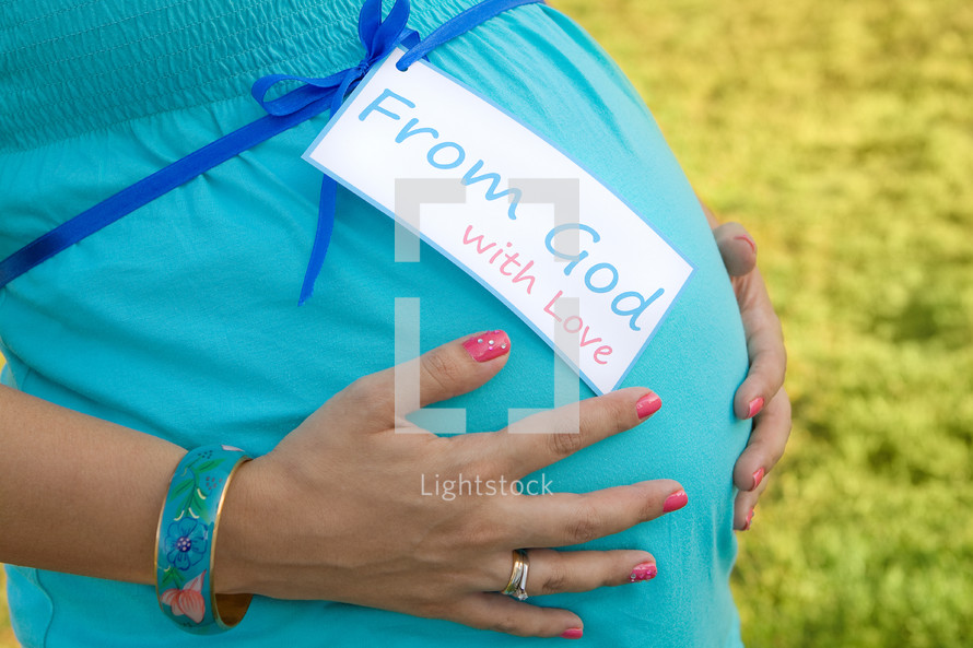pregnant woman with her hands over her belly with a tag - from god with love