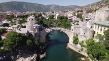 Crowded Mostar Old Bridge with many tourists walking over, aerial establishing	