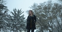 Happy woman model in winter coat standing outside on Christmas watching slow motion snow as snowflakes fall in cinematic slow motion.