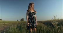 Young woman in summer nature in green grass field outside watching sunset in summer.