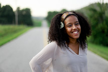 a smiling young woman standing in the middle of a road 