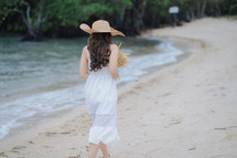 a woman in a white dress walking on a beach 