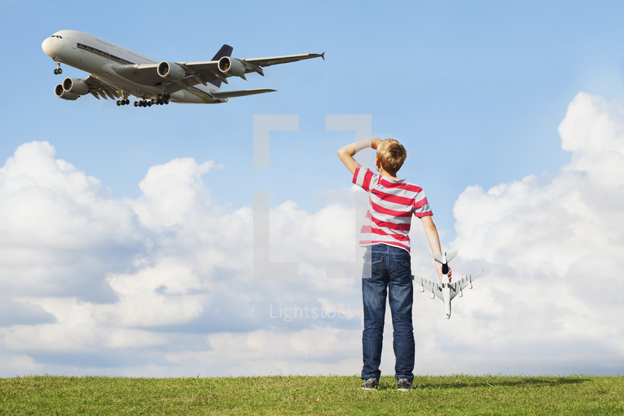 Pre teen caucasian boy holding model plane as a passenger plane flies overhead