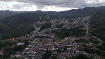 Drone orbits from east to south around city of Ouro Preto on cloudy afternoon