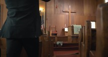 Young, emotional, anxious, and stressed man with long hair and black suit sitting in old church in worship and praying.