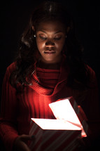 A woman opening a gift box that is glowing inside. 