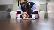 a young woman praying over an open Bible 