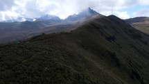 Aerial shot drone follows hikers heading up mountain trail toward volcano