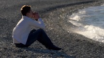 Guy sitting on a rocky shore, praying and thinking. 