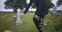 Young, sad man in black suit kneeling in cemetery at graveyard tombstone grieving in cinematic slow motion.