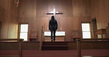 Young man in church walking to wooden cross.