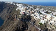Aerial shot drone orbits to the right around cliff at Thera, Santorini