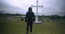Young man in black suit looking at cross praying in worship in cinematic slow motion.