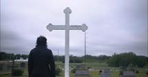 Young man in black suit looking at cross praying in worship in cinematic slow motion.