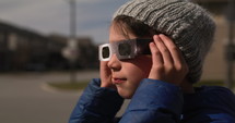 Boy puts on solar glasses and looks up to watch eclipse - side profile