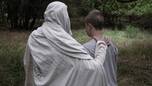 Jesus Christ comforting a young man. Teen boy walking with Jesus in nature in slow motion.