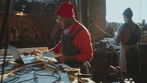 African American Blacksmith Using Laptop and Taking Notes in Workshop