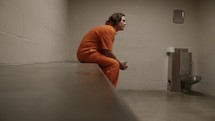 Sad, depressed criminal. Man locked up behind prison bars in his prison cell for criminal activity in cinematic slow motion.