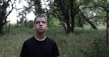 Unhappy young man, teenage boy with black eye walking in forest trees.