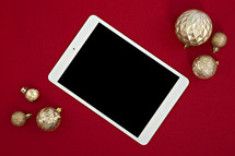 gold Christmas ornaments on a red background and tablet 