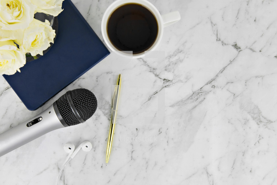 notebook, earbuds, coffee mug, roses, microphone, and pen on a marble background 