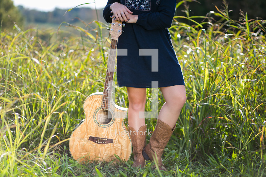 young woman standing in a field with a guitar 