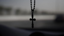 A christian cross hanging inside the windshield of a car driving down the highway.