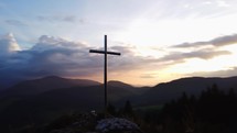 Aerial view of a religious Christian steel cross on a hill in the mountainous countryside, in sunset